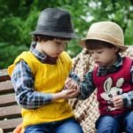 Two Boys Sitting on Bench Wearing Hats and Long-sleeved Shirts