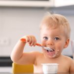 Adorable one year old baby boy eating yoghurt with spoon