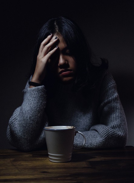 depressed lady sitting with coffee holidng her head